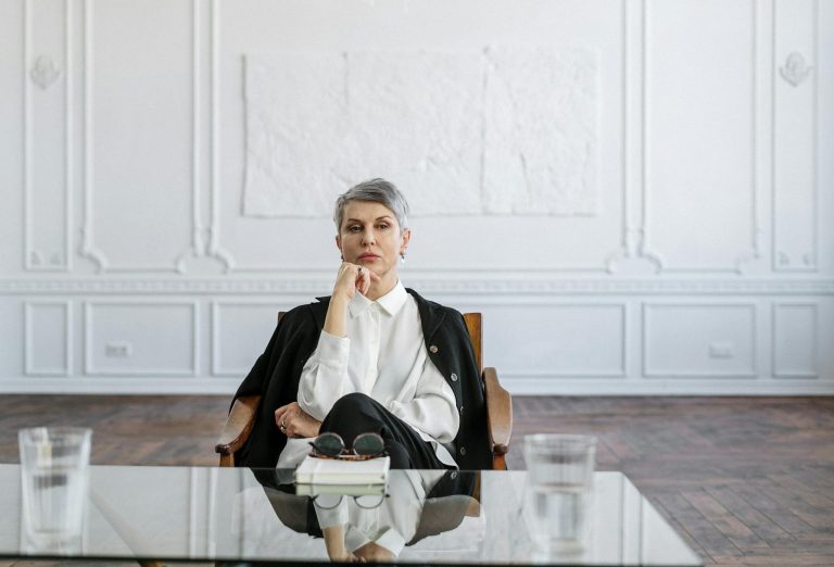 Confident woman in a stylish office sitting at a glass table, symbolizing professionalism and focus.