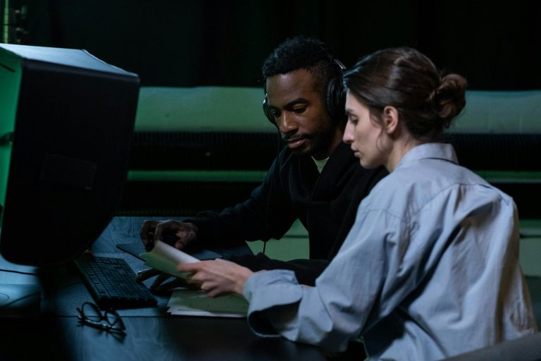 Two colleagues engaged in focused editing work at a computer, collaborating effectively.